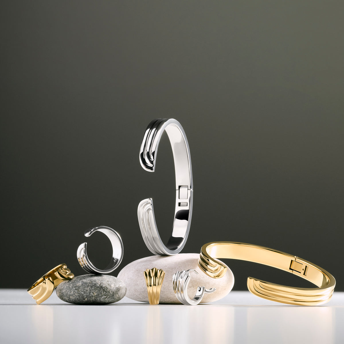 Gold and silver wave bangles, rings and earrings displayed on smooth stones against a dark gray background. Nickel-free, waterproof & tarnish-resistant stainless steel jewelry for sensitive skin, minimalist luxury jewelry by Mia Bijoux.
Joncs, bagues et boucles d'oreilles dorés et argentés à motif vagues présentés sur des galets sur fond gris foncé. Bijoux en acier inoxydable sans nickel, résistants à l'eau et anti-ternissement pour peaux sensibles, bijouterie de luxe minimaliste par Mia Bijoux.