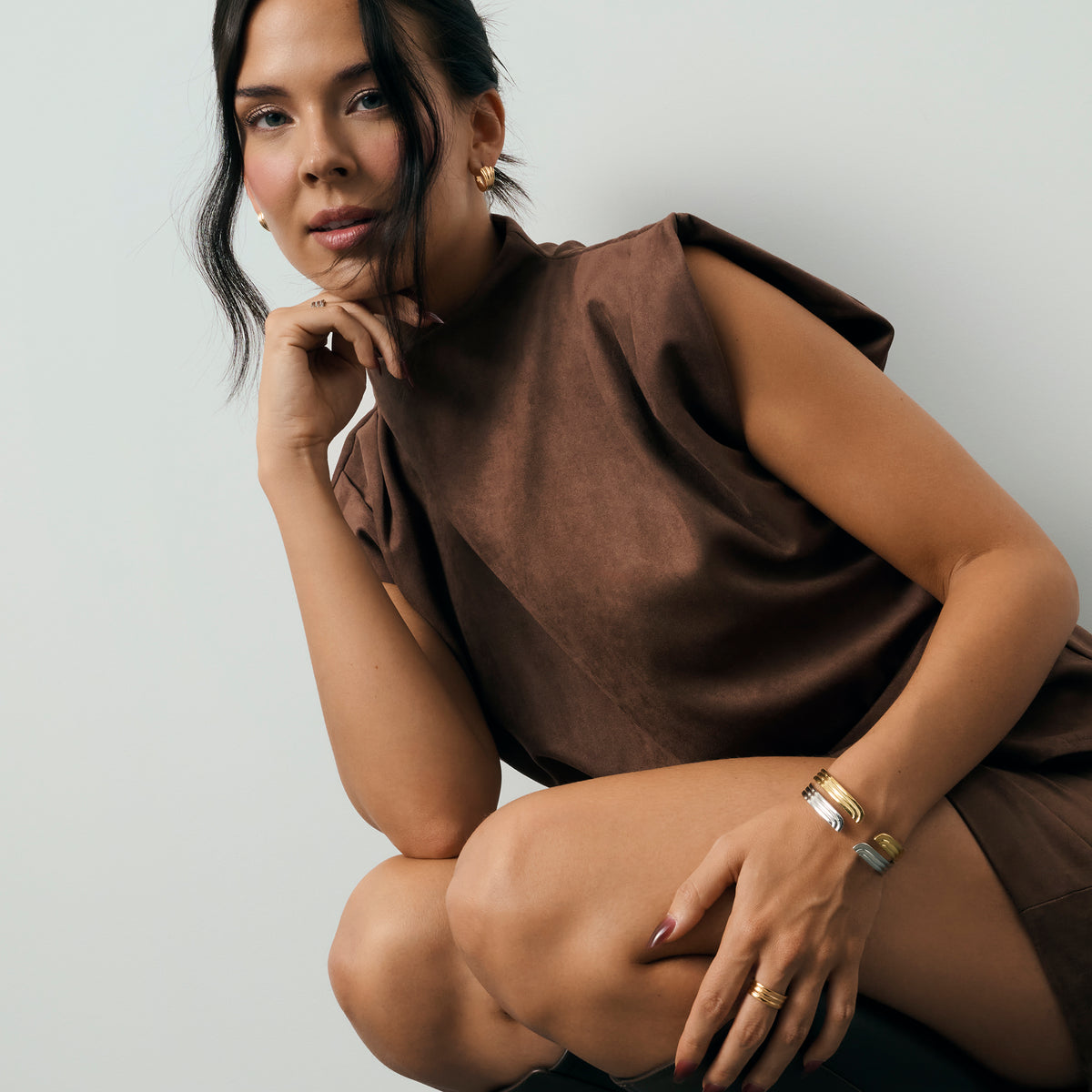 Woman wearing a brown sleeveless top and multiple gold and silver-toned bracelets and rings against a light gray background. Nickel-free, waterproof & tarnish-resistant stainless steel jewelry for sensitive skin.

Femme portant un haut brun sans manches et plusieurs bracelets et bagues dorés et argentés sur fond gris pâle. Bijoux en acier inoxydable sans nickel, résistants à l'eau et anti-ternissement pour peaux.