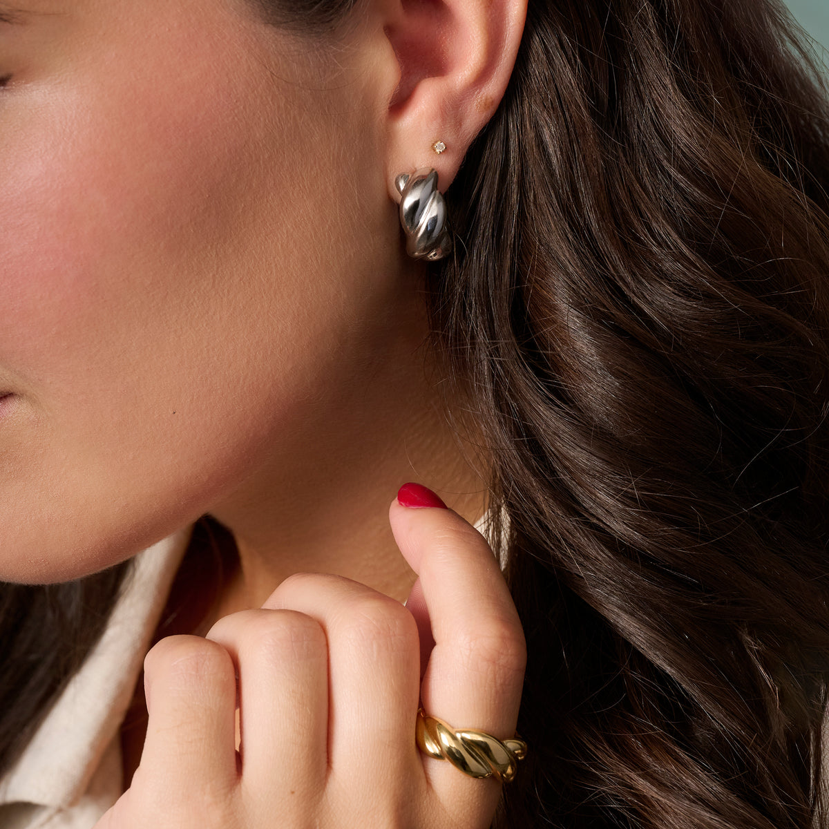 Close-up of a woman wearing a twisted silver hoop earring and a twisted gold ring on her finger, with her hand resting near her neck.

Gros plan d'une femme portant une boucle d'oreille anneau argentée torsadée et une bague dorée torsadée au doigt, la main posée près de son cou.